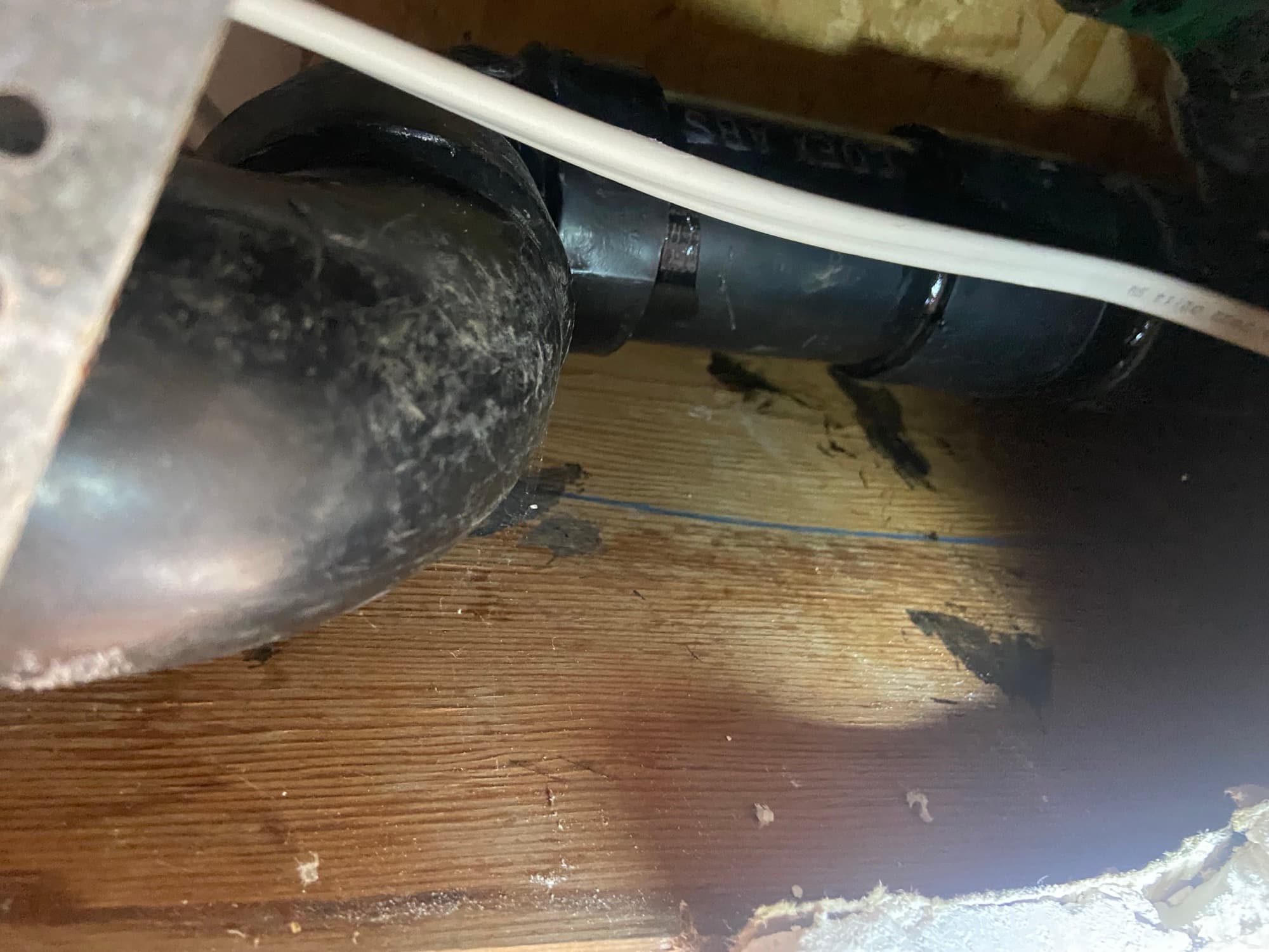 Close-up of an ABS drain pipe fitting installed beneath wood floor joists, Orange County, CA