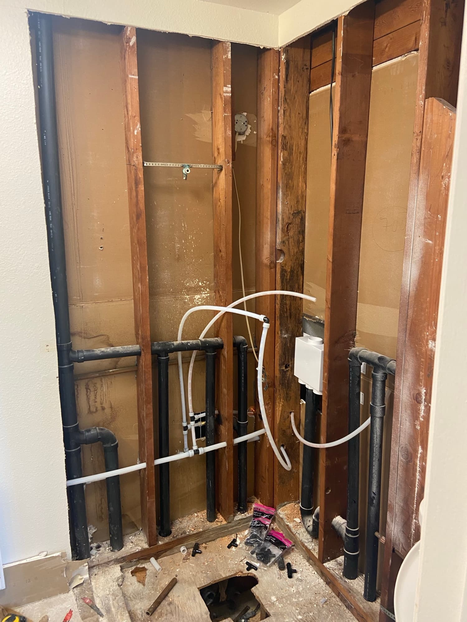 Exposed floor joists with a black ABS drain main line and tape measure, Orange County, CA