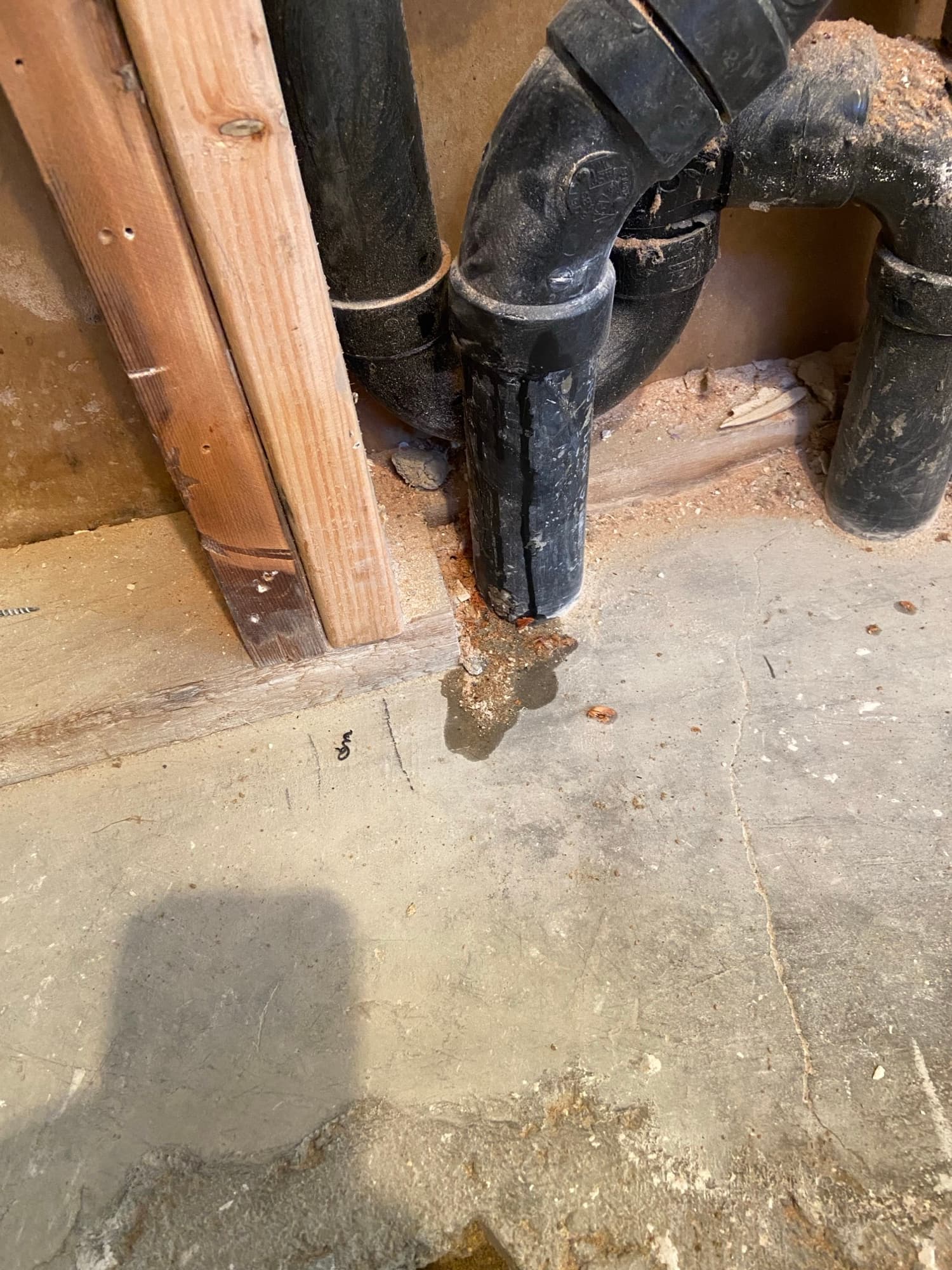 Black ABS drain fitting with elbow joints above a freshly patched concrete slab, Orange County, CA