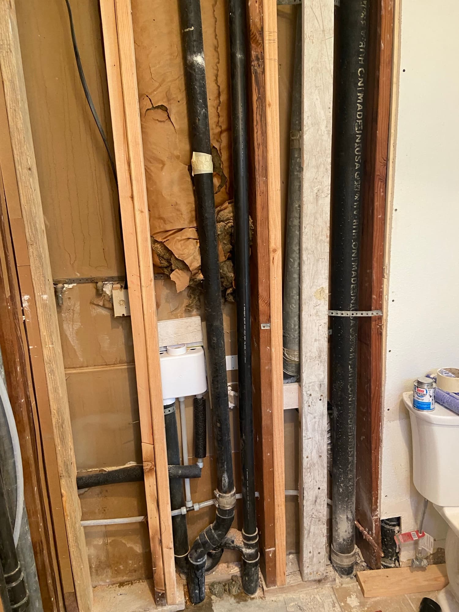 Labeled ABS drain pipes and insulation batts running along wood studs, Orange County, CA