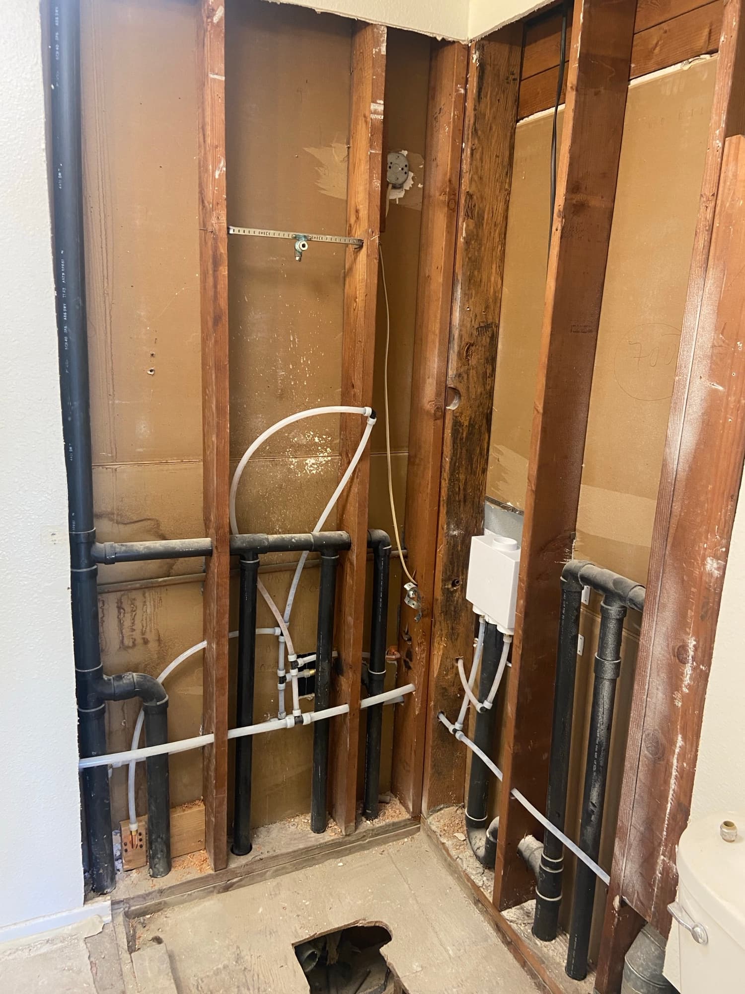 Exposed wall cavity with black drain pipe and PEX lines, Orange County, CA