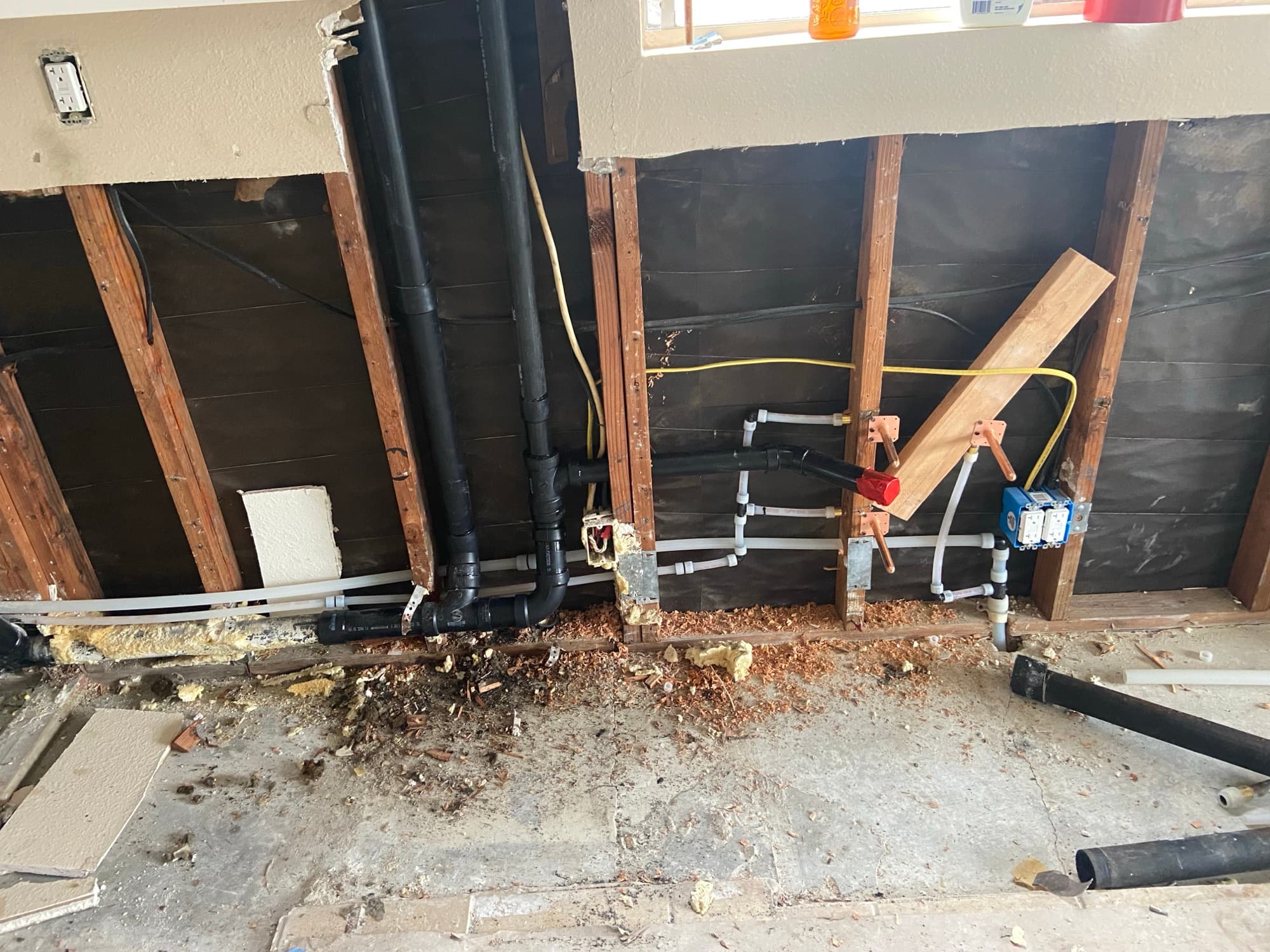 Plumbing rough-in featuring black drain pipe, copper stub-outs, and a red-capped shutoff valve, Orange County, CA