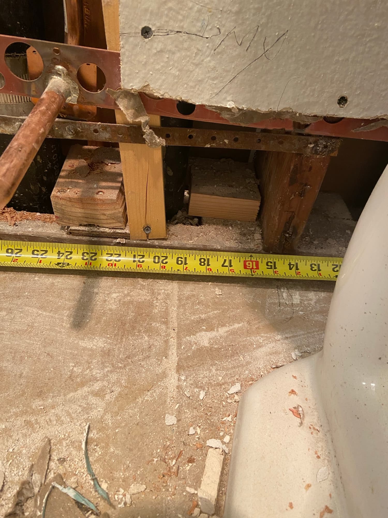 Subfloor opened beneath a toilet base with a tape measure for repipe planning, Orange County, CA